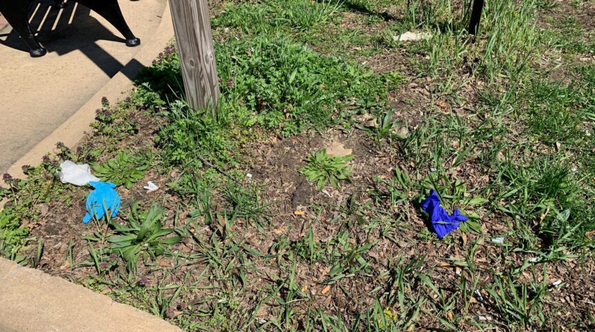 A pair of blue gloves on the ground next to a fence.