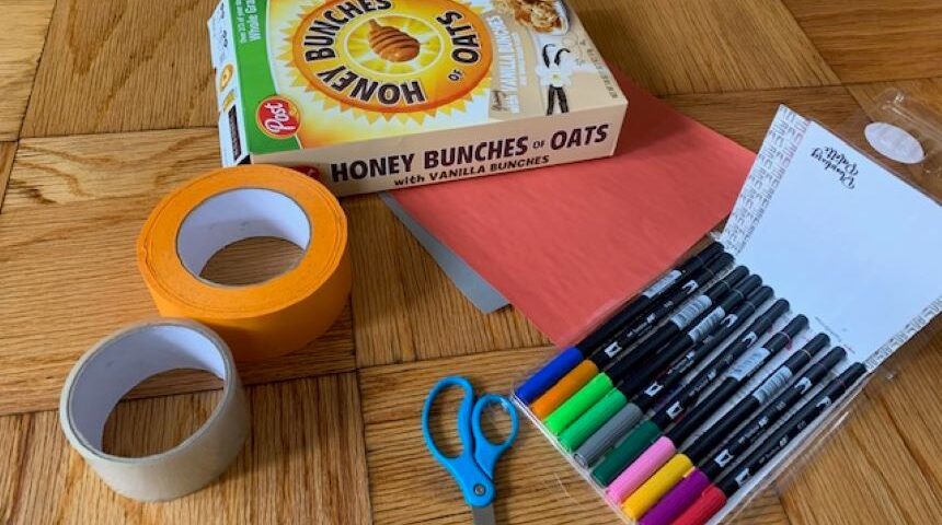 A box of tape, scissors, and markers are on a wooden floor.