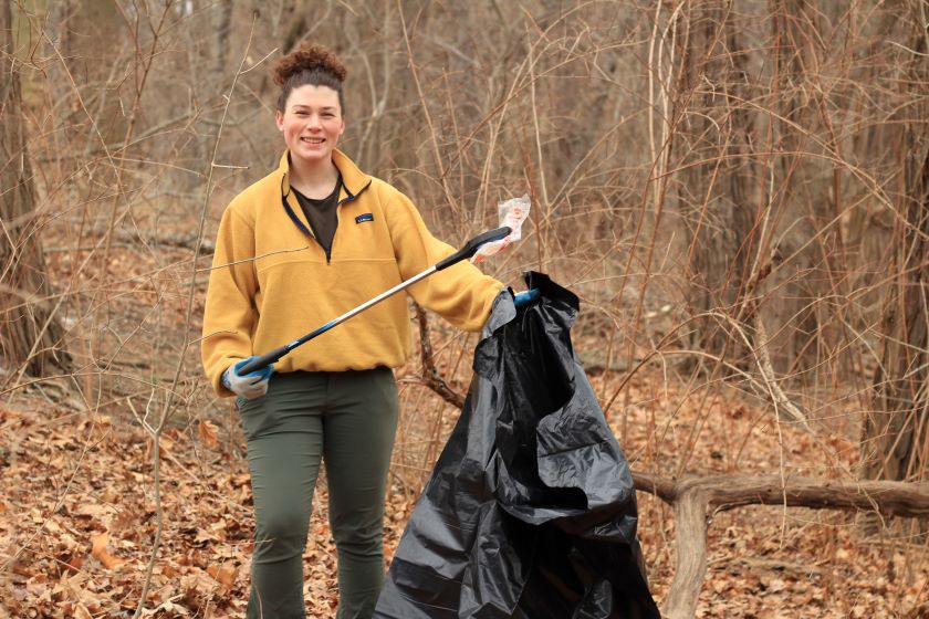 A woman holding a trash bag in the woods.