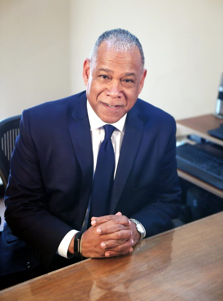 A black man in a suit sitting at a desk.