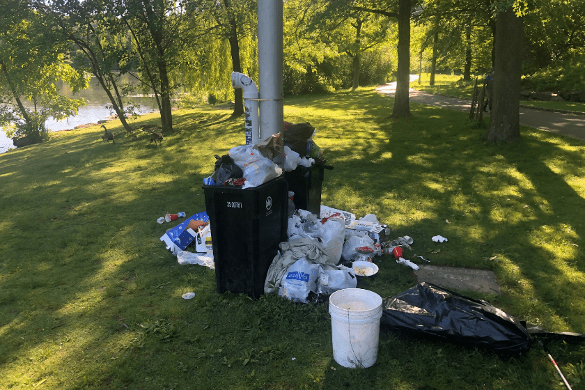 A trash can on a grassy area near a lake.