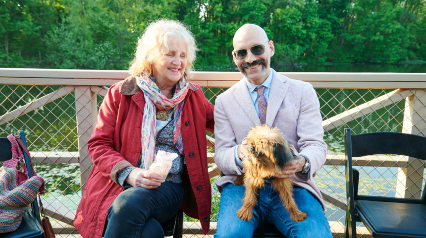 A man and woman sitting on a bench with a dog.
