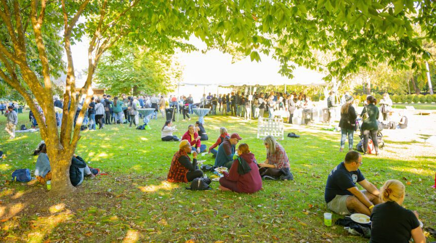 A group of people sitting on the grass under trees.