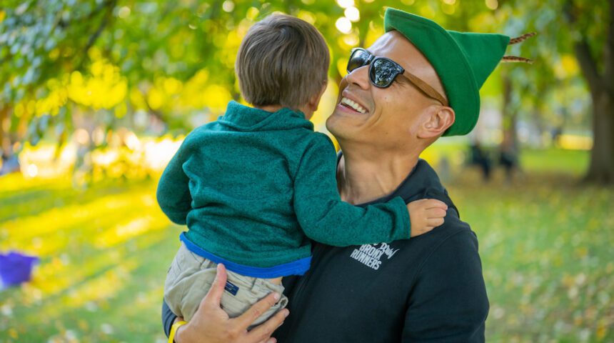 A man with a green hat holding a child in a park.