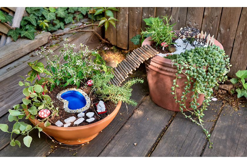 A fairy garden in a pot on a wooden deck.