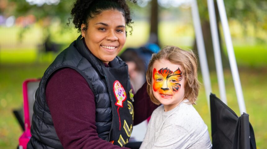 A woman is painting a child's face at an outdoor event.