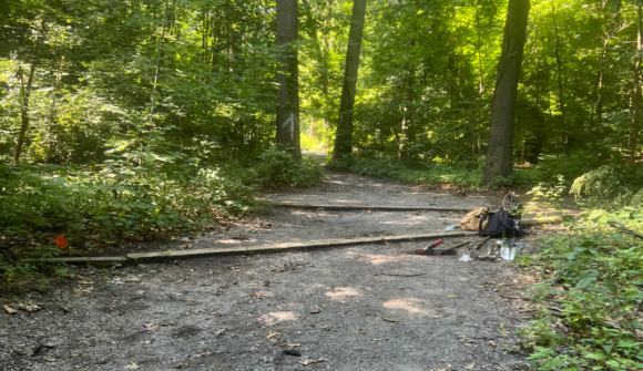 A trail in the woods with stone surface and wooden bars with a pile of tools and bags.