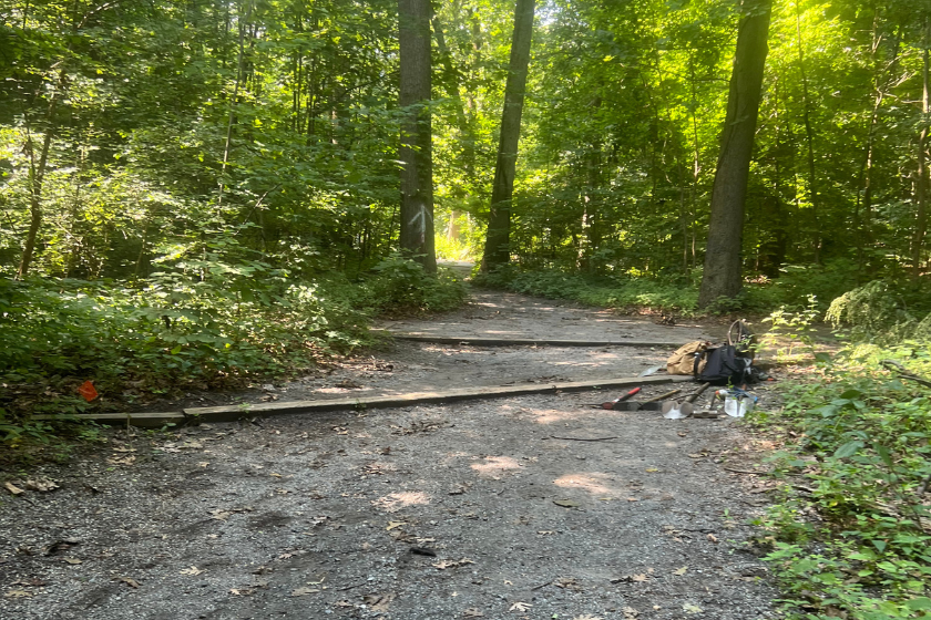 A trail in the woods with stone surface and wooden bars with a pile of tools and bags.