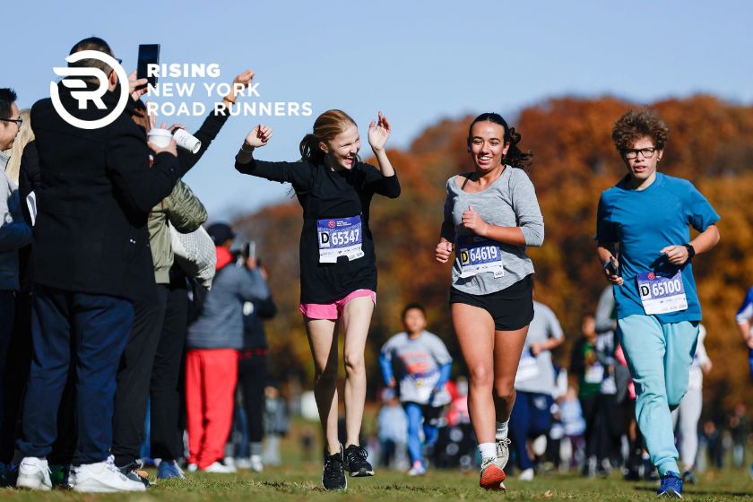 Three young people running outside with fans cheering them on.