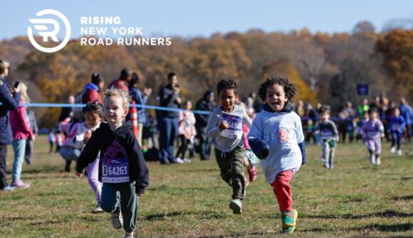 Young children running with smiles across a grassy field.