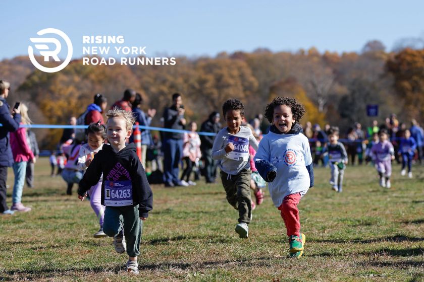 Young children running with smiles across a grassy field.