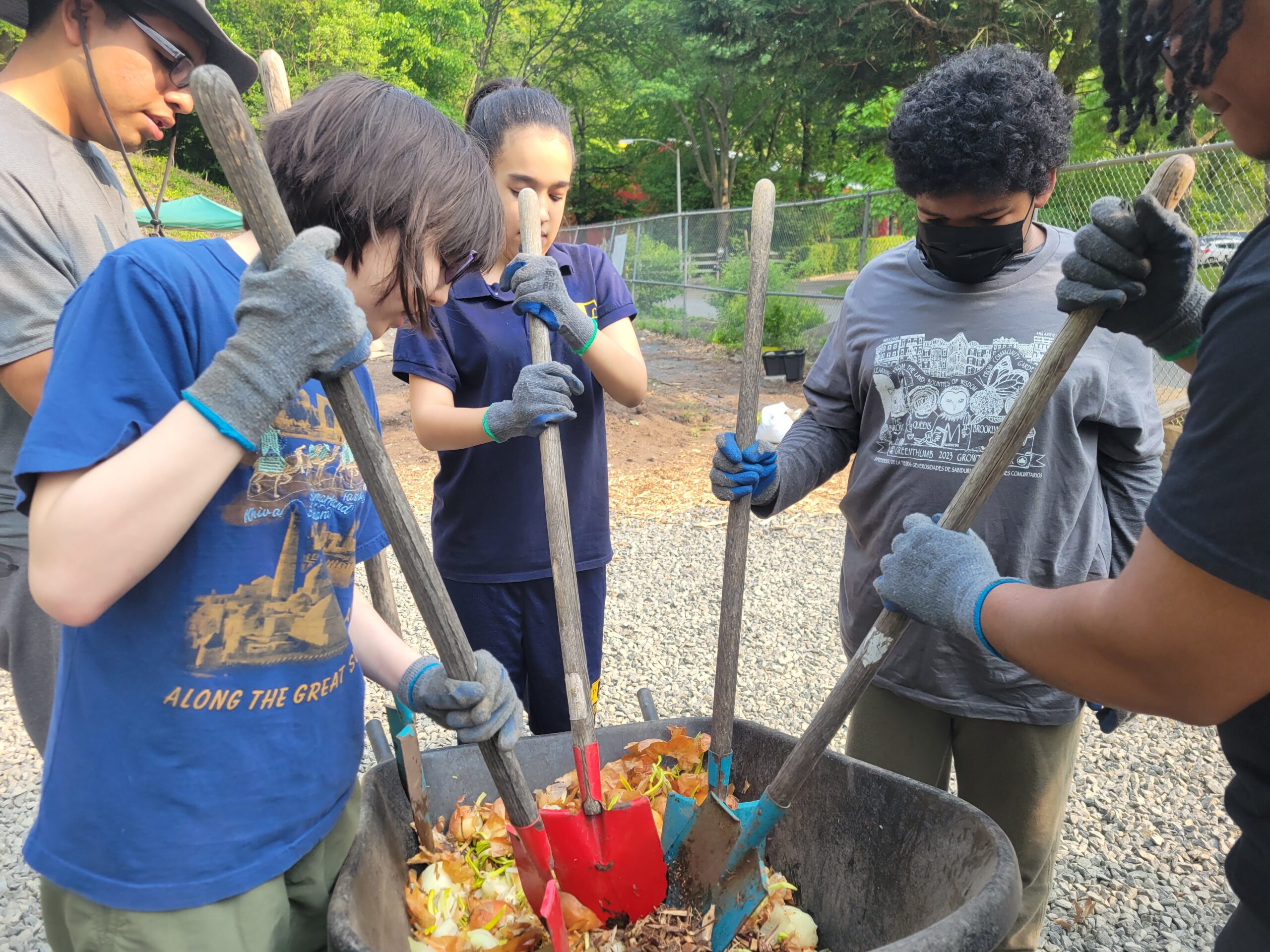 A group of people holding shovels and digging in a wheelbarrow full of leaves.