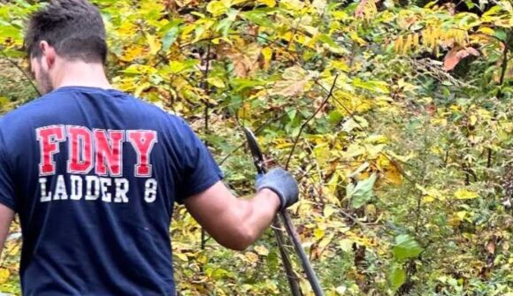 A person standing in a shrub area holding loppers.