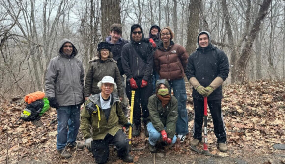 A group of people in the forest bundled up and holding work tools.