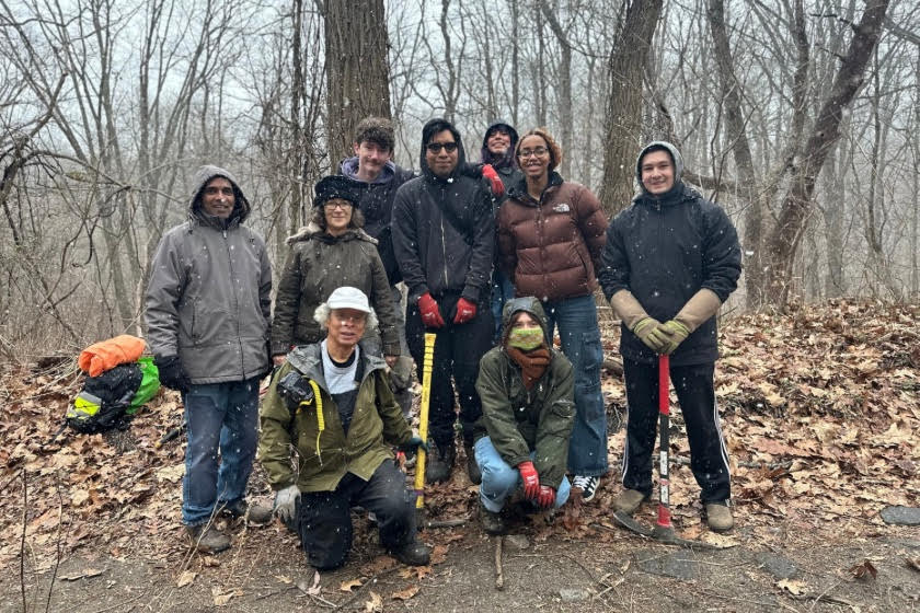 A group of people in the forest bundled up and holding work tools.