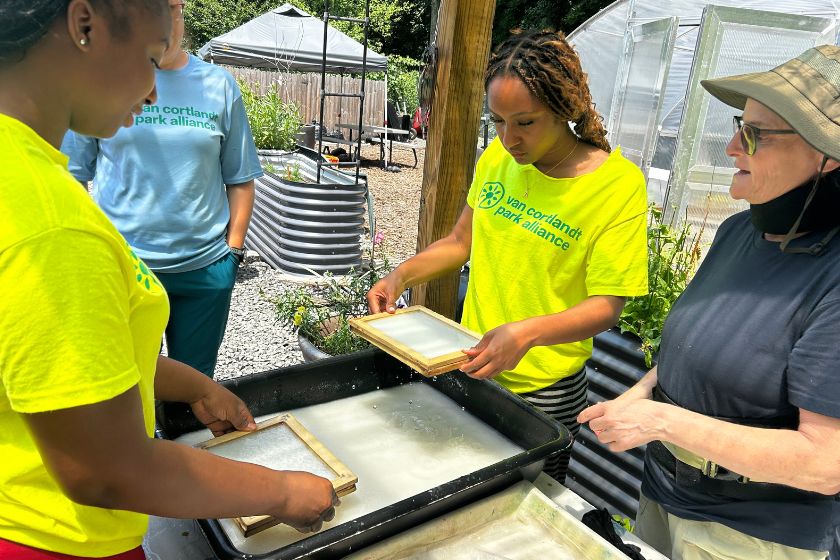 Two young ladies in bright yellow shirts using screens to make paper with two other women looking on.