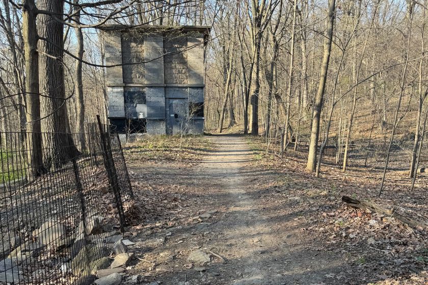 A trail in the woods during winter with no leaves on the trees and a concrete structure along the trail - the weir.